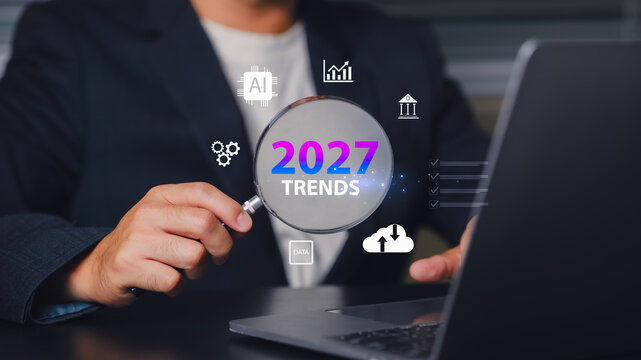 Business professional analyzing digital data trends 2027 using a magnifying glass and online icons related to technology and finance, emphasizing growth and strategy.