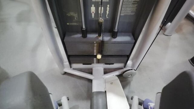 Close-up view of a metal weight stack on a gym strength training machine. Features black plates with a yellow selector pin, guide rods, and muscle target diagrams. Fitness and bodybuilding concept.