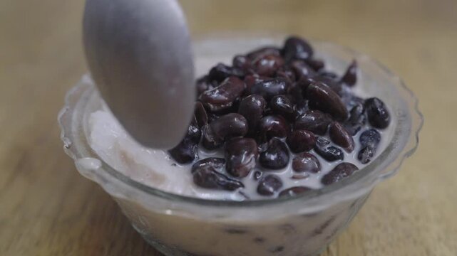 Close-up of traditional Asian dessert with sweet black beans served in creamy coconut milk in a clear glass bowl on a wooden table. Delicious and healthy oriental sweet snack or breakfast dish.