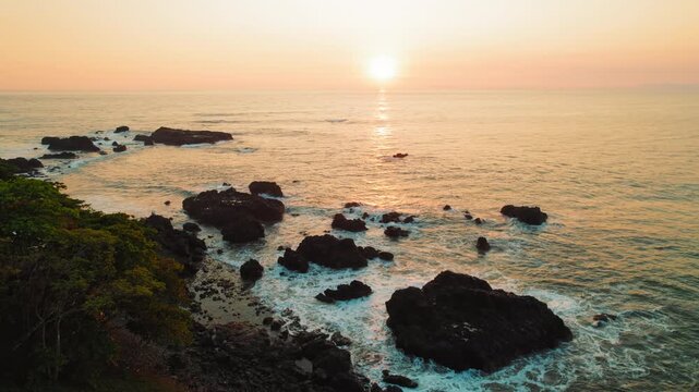 Sunset over rocky shoreline with golden light on ocean near Jaco, Costa Rica