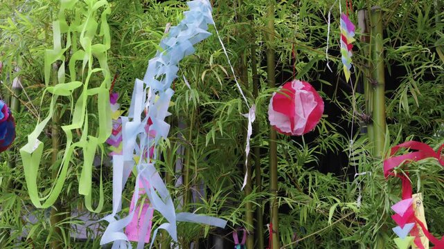 Japanese Tanabata Star Festival decorations hanging on lush green bamboo branches. Features colorful paper streamers, handmade ornaments, and wishing tags in a vibrant outdoor summer display.