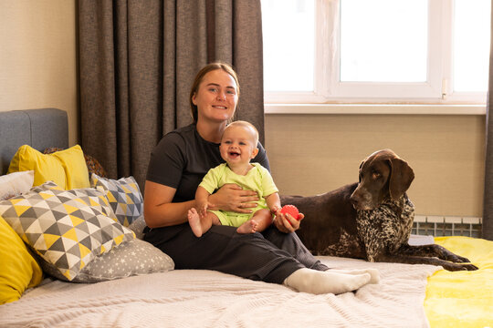 Smiling Mother Holds Baby and Red Ball Beside Pointer