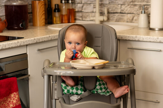 Curious Baby Boy Chews Toy In Kitchen High Chair