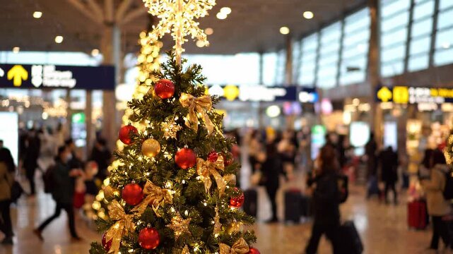 A festive Christmas tree in a busy airport terminal, surrounded by blurred travelers, captures the holiday mood.