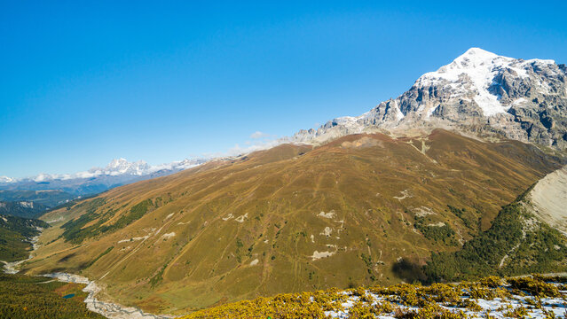 Landscape photograph of wide Adishi valley with snow covered peak viewed from Chkhutnieri pass in Svaneti Georgia.
