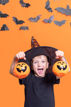 Boy in a hat holding a halloween pumpkin in front of his head on an orange background with paper bats, vertical