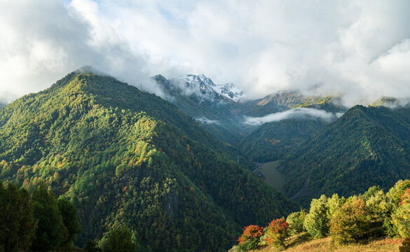 Landscape photograph of lush autumn mountain slopes with low clouds and snow peaks in Svaneti Georgia.