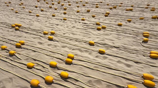 Wide shot of many Yellow Buoys rows on Ropes stretched Over Rippled Sand Beach