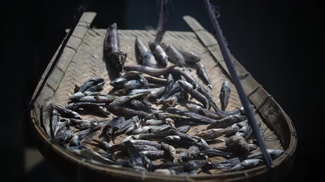 Close-up of sun-dried fish laid out on a woven bamboo basket in a countryside setting.