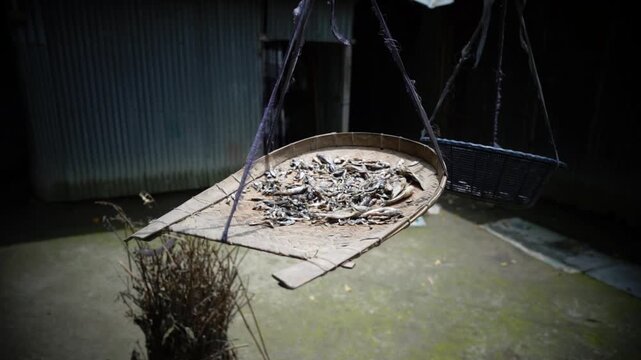 Close-up of sun-dried fish laid out on a woven bamboo basket in a countryside setting.