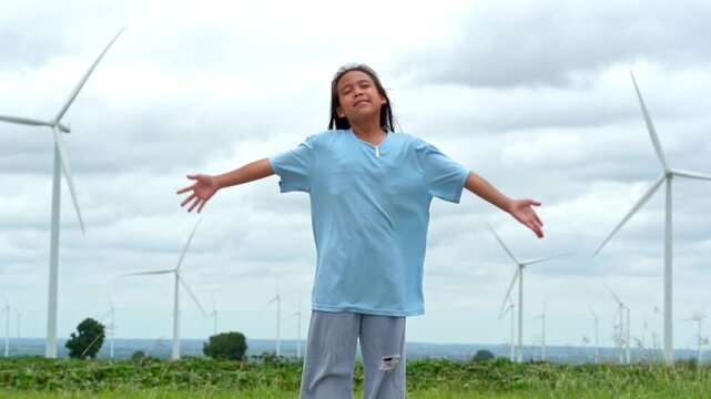 Happy young girl standing with open arms embracing nature with wind turbines in background