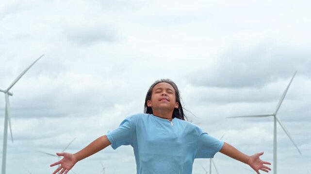 Happy young girl standing with open arms embracing nature with wind turbines in background