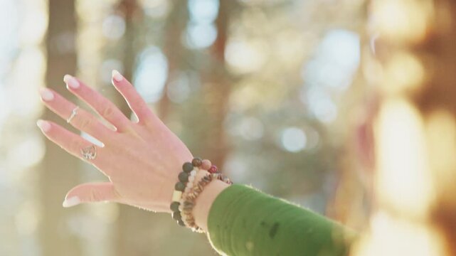 Hand reaches toward warm sunlight through forest. Fingers gently open, catching golden rays. Soft focus on blurred trees behind. Calm, peaceful, hopeful moment captured. Ideal for wellness, meditation