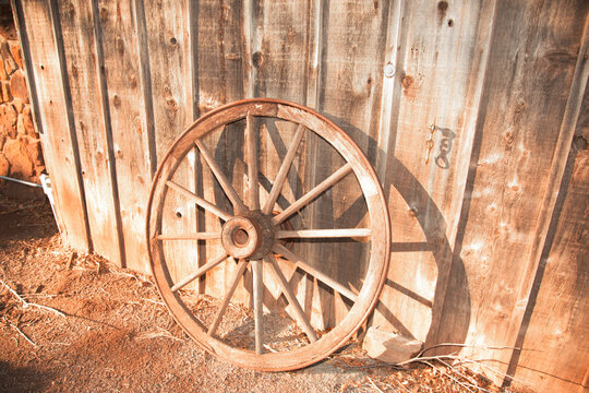 An authentic old wooden wagon wheel leaning against a weathered rustic barn wall, showcasing vintage country charm and historical farm aesthetics.
