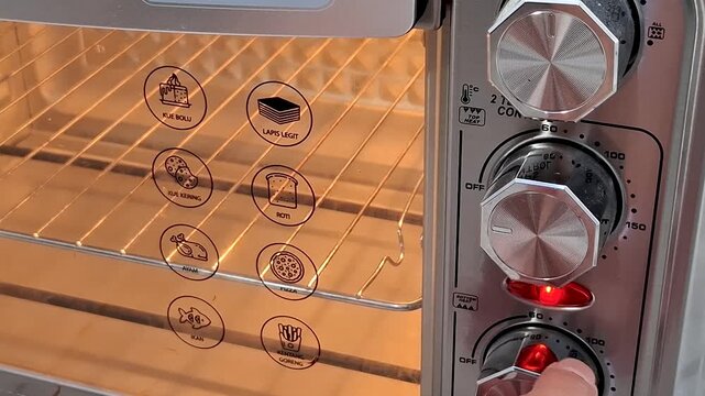 Close up of a toaster oven with glowing interior showing cooking preset icons and a hand adjusting the temperature control dial