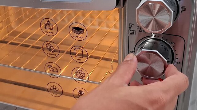 Close up of a hand turning a knob on a toaster oven with glowing heating elements The oven interior displays icons for various food items
