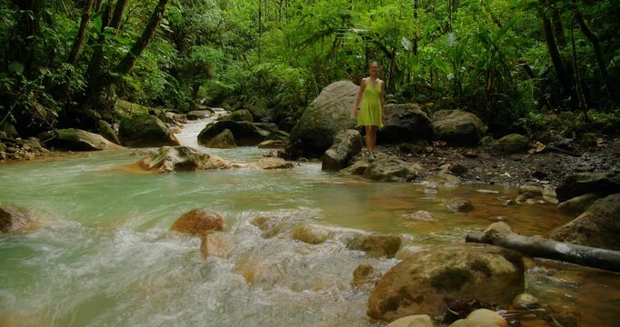 Woman walks beside turquoise river rocks in Blue Falls during travel in Costa Rica