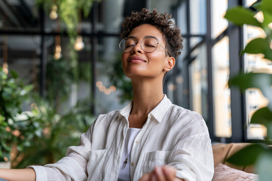 Young woman rests peacefully with eyes closed. She wears glasses and a light-colored shirt. Her curly hair frames her serene expression. Sunlight filters through tall windows behind her