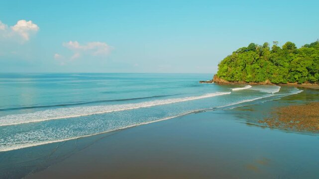 Wide sandy beach borders a dense tropical forest under a clear blue sky in Costa Rica