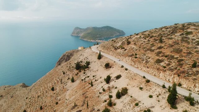 Car driving on a coastal mountain road leading to peninsula with a view of Asos village below in Kefalonia, Greece