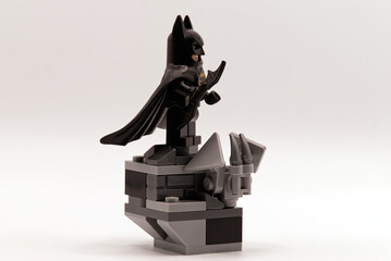 Fototapeta premium Bologna - Italy - August 19, 2026: Lego batman minifigure standing on a grey stone gargoyle ledge holding a batarang weapon.