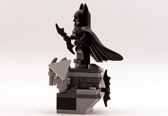 Fototapeta premium Bologna - Italy - August 19, 2026: Lego batman minifigure standing on a grey brick built gargoyle ledge holding a batarang weapon on white background.