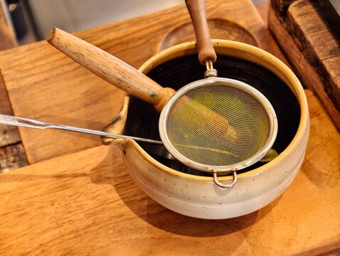 A close-up view of traditional matcha green tea tools, featuring a fine mesh sifter and metal scoop on a handcrafted ceramic bowl. Perfect for tea ceremony, cafe menu, and healthy drink concepts.