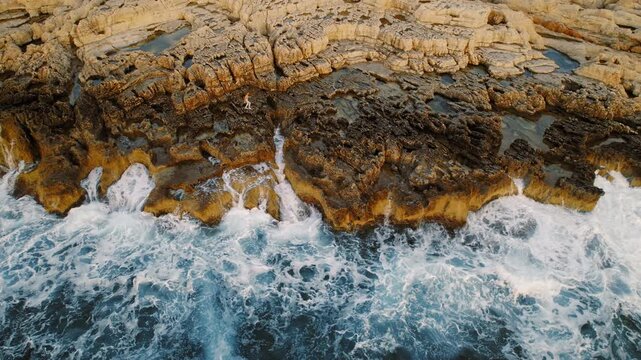 Person climbing rugged coastal rocks above crashing ocean waves at sunset