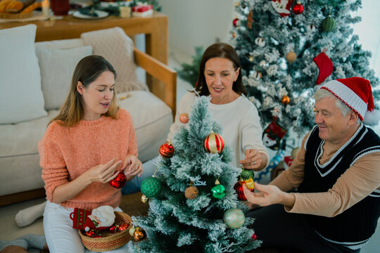 Multigenerational family placing ornaments on Christmas tree together at home, sharing joyful holiday tradition, bonding, happiness, festive celebration.