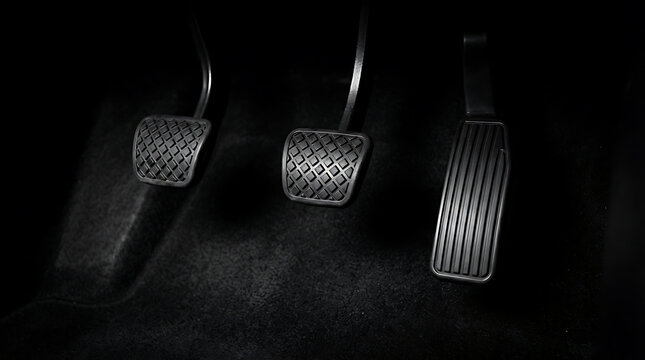 Car pedals in dark footwell, manual transmission clutch brake and accelerator controls.