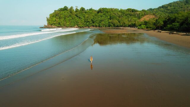 Tourist woman walks on wide sandy shore with reflection of green jungle hills