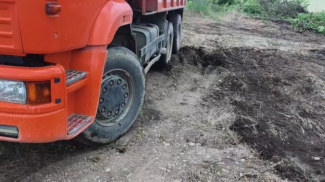 Orange truck parked on a muddy rural path with disturbed soil and overgrown vegetation. Nature reclaiming abandoned infrastructure for environmental restoration projects.