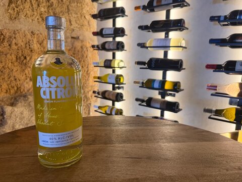 Palma, spain, august 2, 2026, absolut citron vodka bottle displaying its yellow liquid and label, contrasting with a stone wall and wine racks