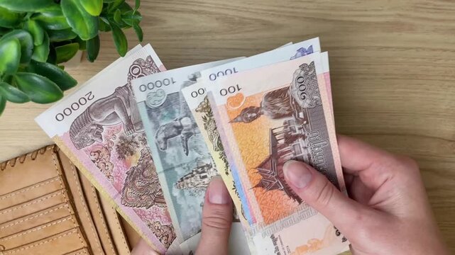 A close-up of a woman's hands counting Cambodian riels at a table. Conceptualizing tourist expenses, budgeting, and using local currency while traveling in Cambodia.