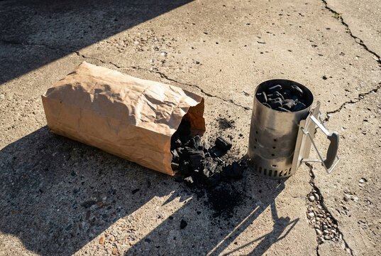 Person preparing barbecue with charcoal on concrete surface.