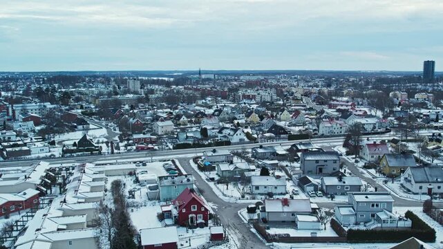 Drone view across a Swedish city in winter showing snow covered homes residential streets and buildings under a cold Nordic sky