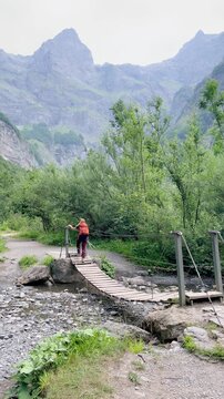 hiker crossing wooden bridge over stream in mountain valley landscape, Alps in France, vertical video