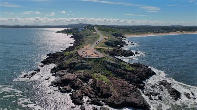 A scenic aerial view of Punta Ballena, a rocky peninsula with a narrow road cutting through the Atlantic coastline on a sunny day.