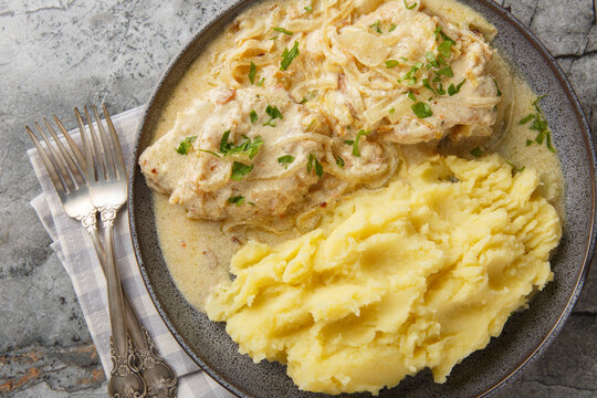 Juicy German schnitzel with onion cream sauce and served with mashed potatoes close-up in a plate on the table. Horizontal top view from above