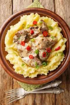 Chicken liver in cream sauce with mashed potatoes closeup on thr plate on the wooden table. Vertical top view from above