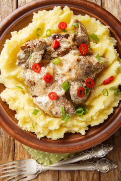 Fried chicken liver with cream sauce with mashed potatoes closeup on thr plate on the wooden table. Vertical top view from above