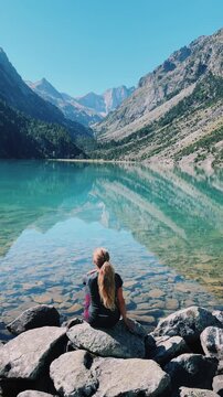 woman sitting on rocks looking at turquoise alpine lake reflection in mountain valley, Gaube lake in France
