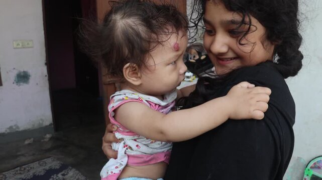 Indian sisters sharing a loving moment outdoors, with an older girl holding her younger sister close as they smile and look at each other.