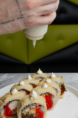 Tattooed hand adding creamy sauce to sushi rolls © Cavan