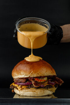 Pouring melted cheese on a gourmet bacon burger