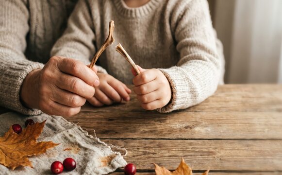 Elderly woman and young child breaking a turkey wishbone together at a rustic wooden table with autumn leaves and cranberries for Thanksgiving tradition.