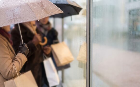 People with umbrellas and shopping bags looking at a shop window on a rainy day
