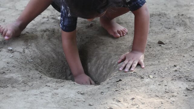 Indian child playing barefoot in the soil, digging a hole with hands outdoors, depicting rural childhood, curiosity, exploration, innocent play, and traditional village lifestyle.