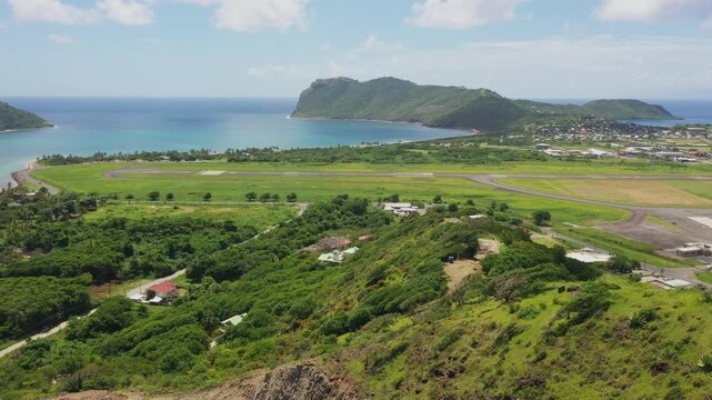 Aerial view of Vieux Fort, Saint Lucia, with Hewanorra Airport's runway winding along the coast, framed by verdant hills, tropical foliage, and the majestic Moule &agrave; Chique cliffs.