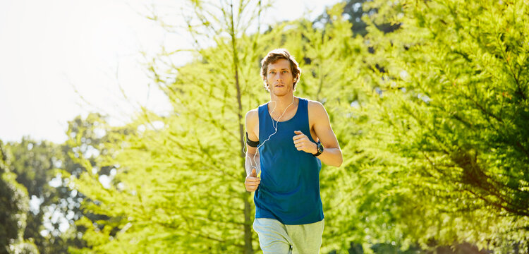 Man, running and outdoor with earphones for training, fitness or streaming music with cardio wellness. Runner, jogging or tech in park for radio, exercise tips podcast or serious for heart health